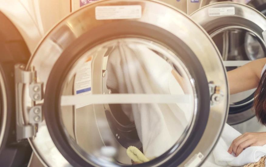 A person places white laundry into a front-loading washing machine at a laundromat.