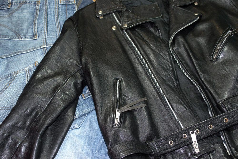 A black leather jacket with zippers lies on top of a pair of blue denim jeans.